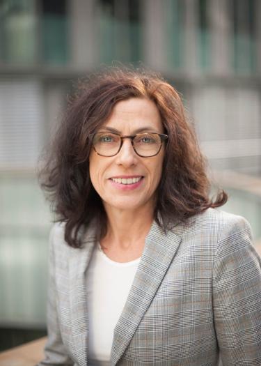 Brünette Frau mit mittellangem Haar und Brille in hellem Blazer