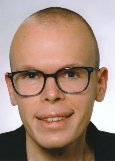 Glatzköpfiger Mann mit dunkler Brille in dunklem Hemd